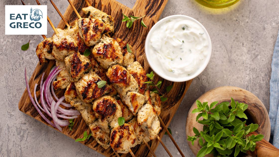 Greek chicken souvlaki with tzatziki sauce, fresh sliced onion and herbs on a wooden platter