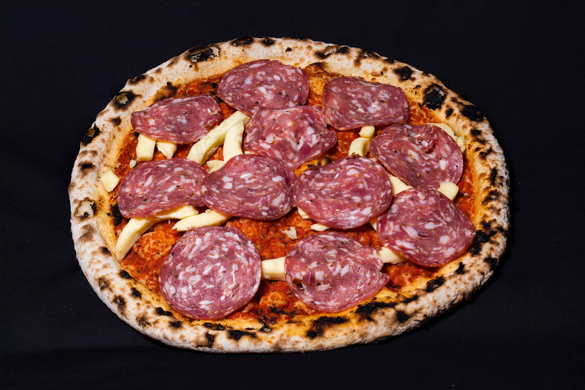 A wood-fired pizza with fresh sliced salame and mozzarella cheese, on a black background.