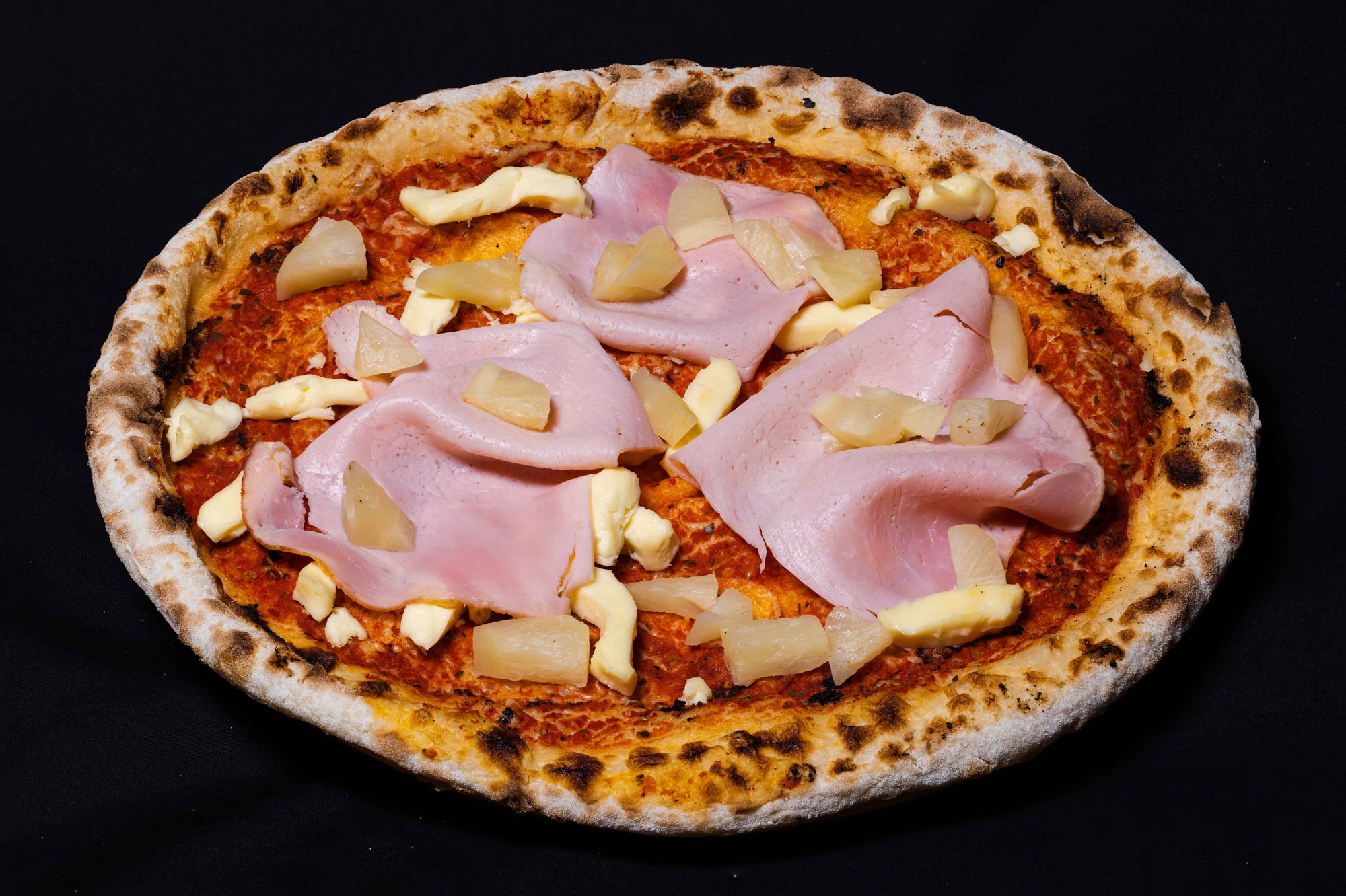 A freshly made Wood-Fired Pizza with toppings of pineapple, ham, and mozzarella cheese, presented on a dark background.
