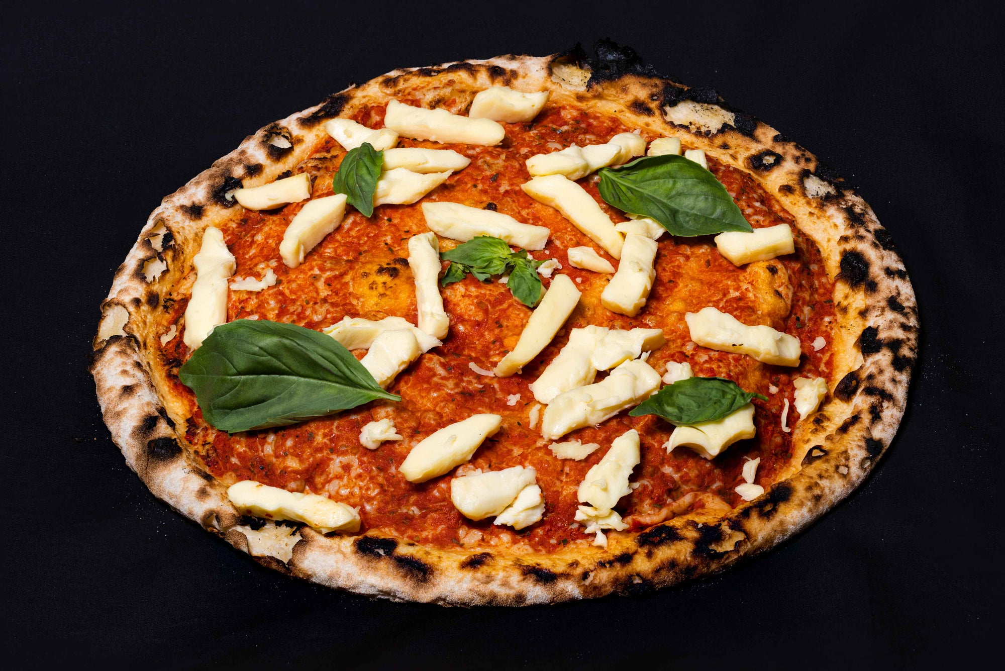 A wood-fired pizza with tomato sauce, fresh mozzarella cheese and fresh basil leaves on a dark background.