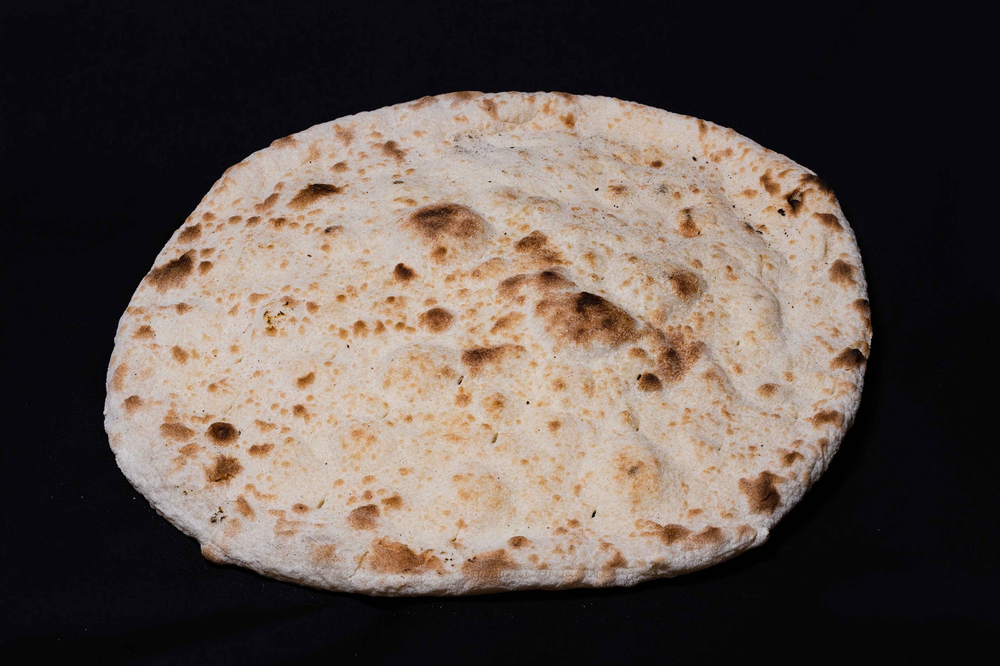 A plain wood-fired pizza base on a dark surface.