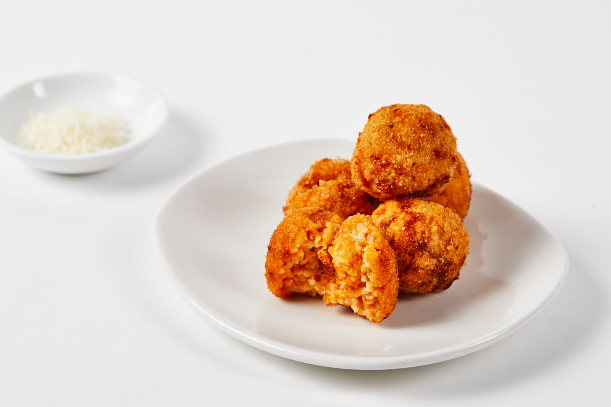 Arancini serve on a white plate with a small bowl of seasoning in the background.